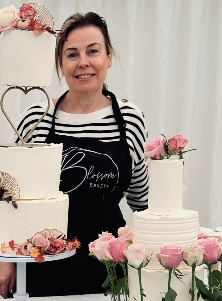 Helen Desmond, owner of Blossom Bakery, in her Blossom Bakery apron beside two of her wedding cakes.